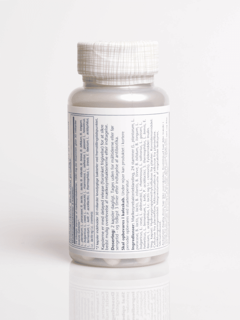 Hvid kosttilskudsflaske med gittermønstret låg, detaljeret dansk label og synlige tabletter i bunden, på hvid baggrund