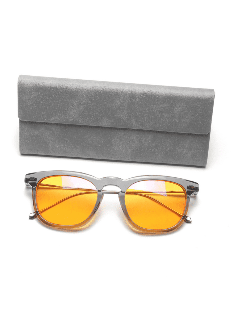 Retro solbriller med orange linser og gennemsigtigt gråt stel placeret foran blødt gråt etui