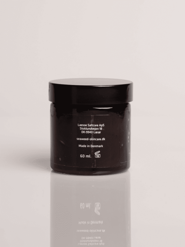 Brun glaskrukke med sort låg, hudplejecreme 60 ml fra dansk seaweed-skincare, reflekteret på blank overflade