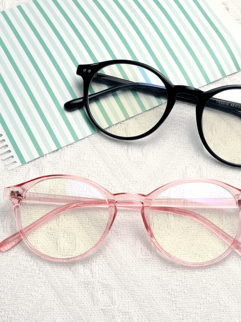 Sort rundbrille og gennemsigtig rosa rundbrille på hvid strikket baggrund ved grønstribet papir