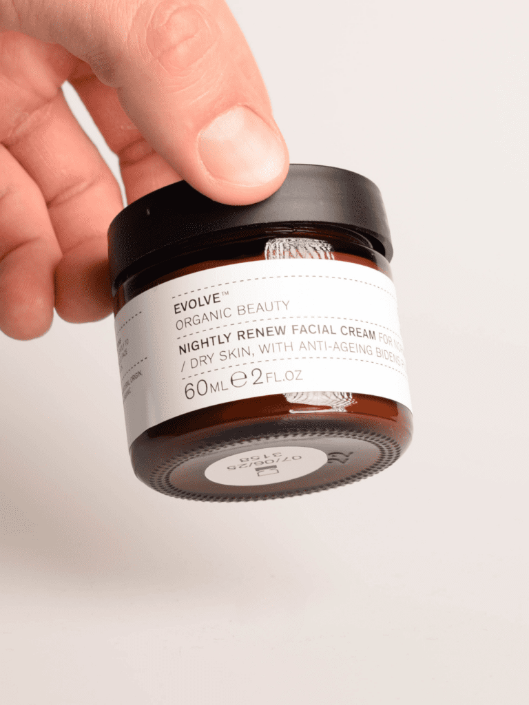 Hånd der holder brun kosmetikkrukke med sort låg og label Evolve Nightly Renew natcreme 60 ml